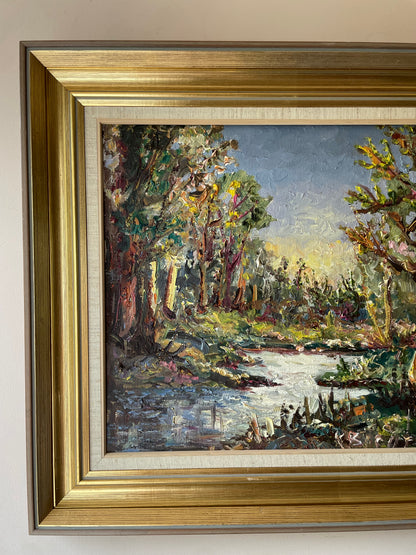 Impasto oil painting of a sunlit woodland stream framed by trees under a pale blue sky, in a gold gilt frame