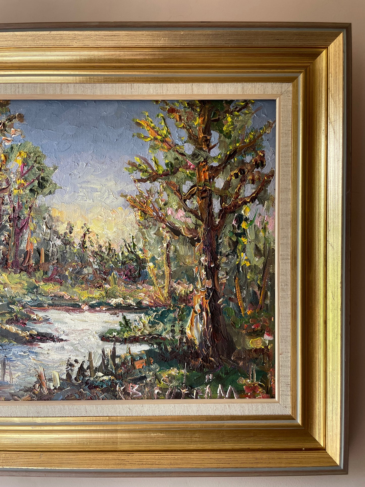 Impasto oil painting of a sunlit woodland stream framed by trees under a pale blue sky, in a gold gilt frame