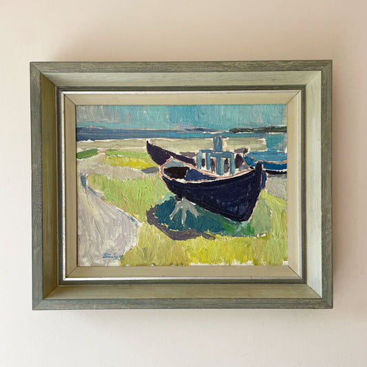 Mid-century Swedish oil painting of two blue fishing boats beached on green grass beside a turquoise sea, in a silvered grey-green wooden frame.