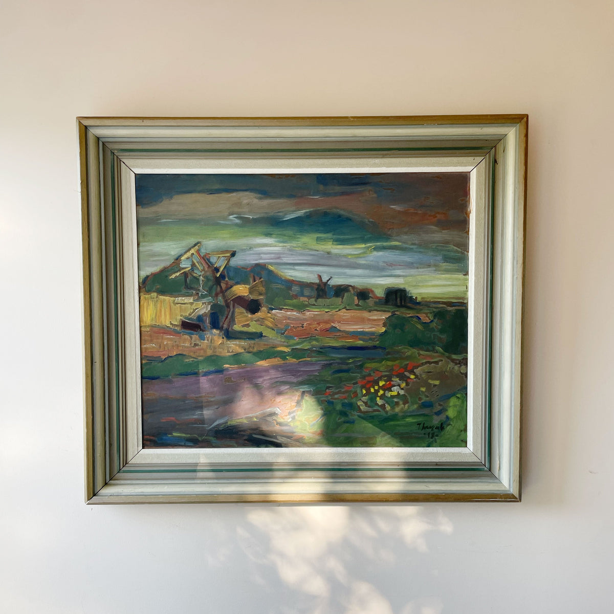 Vintage expressionist landscape oil painting of a harvest scene with a horse-drawn rake and sheaves in fields of green, ochre and purple under a moody sky, in a silver and green wooden frame.