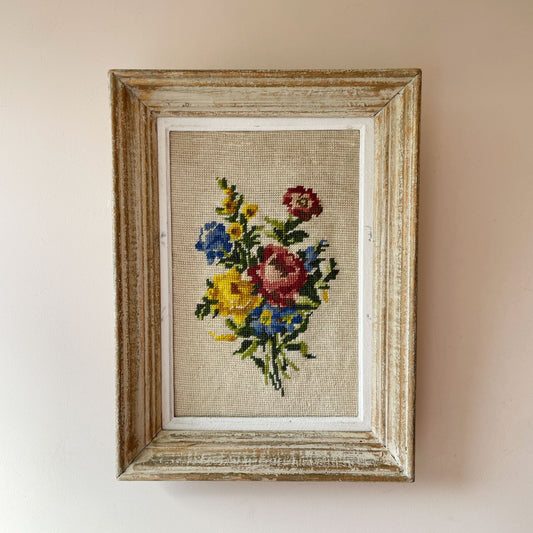Vintage French needlepoint of vibrant floral bouquet with blue sprigs and green leaves on oatmeal, in distressed frame