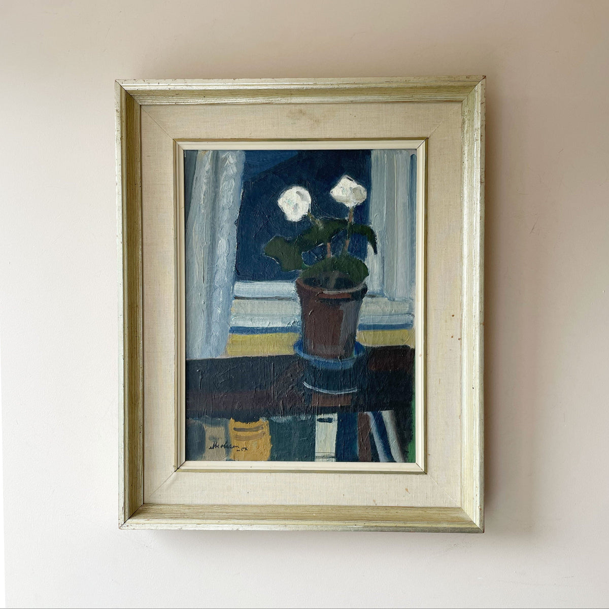 Mid century oil still life of a potted plant with two white flowers on a windowsill against a deep blue interior, in a linen frame