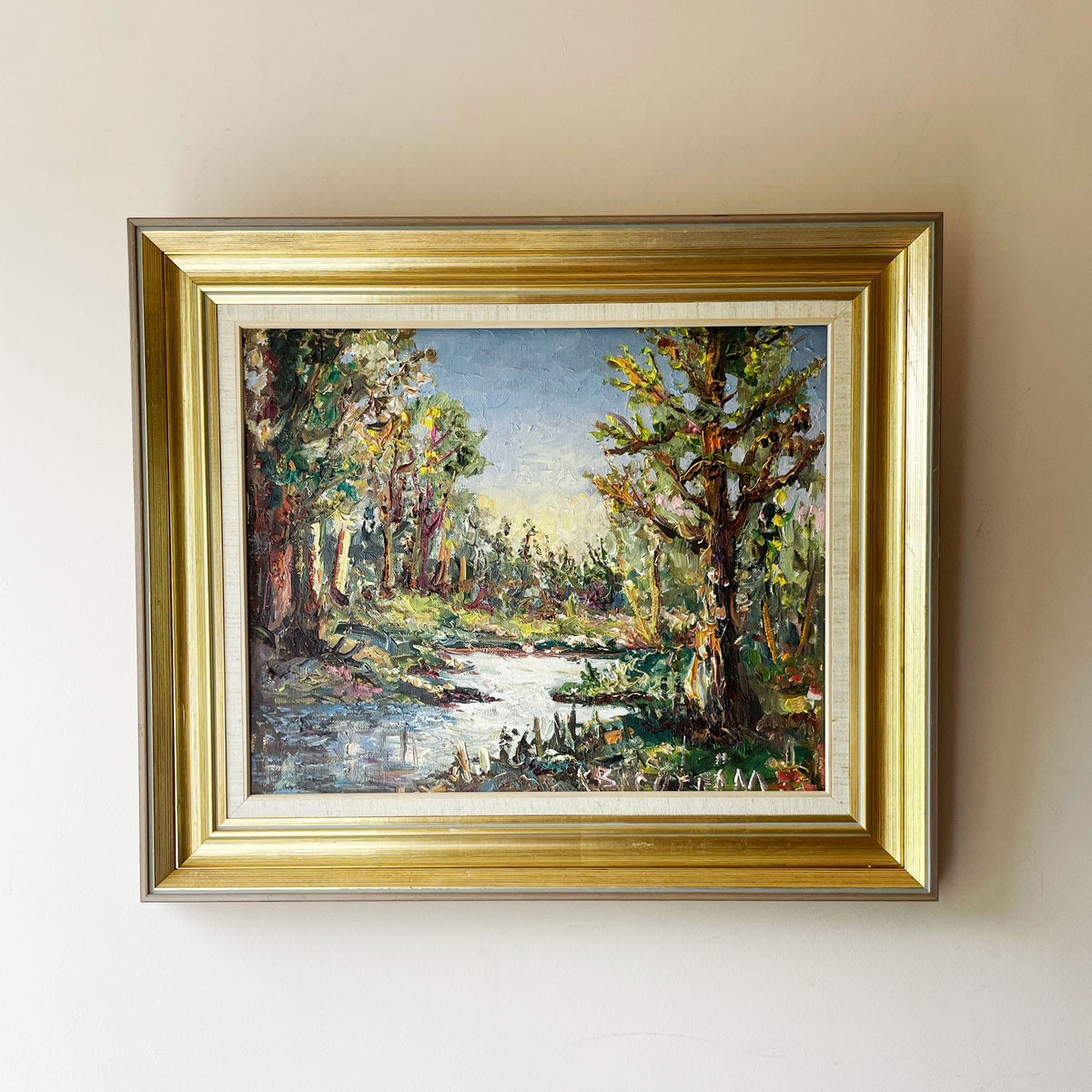 Impasto oil painting of a sunlit woodland stream framed by trees under a pale blue sky, in a gold gilt frame